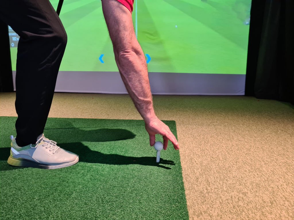 Golfer preparing to tee off indoors, with a golf simulator screen in the background, showcasing the convenience of indoor golf.