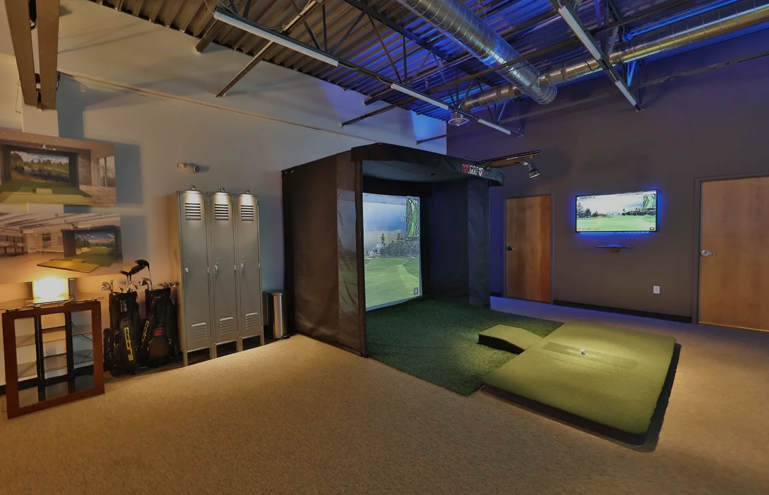 Indoor golf simulator setup featuring a hitting area with artificial turf, projection screen displaying a golf course, lockers for equipment storage, and a television for gameplay visuals, ideal for enhancing home golf practice experiences.