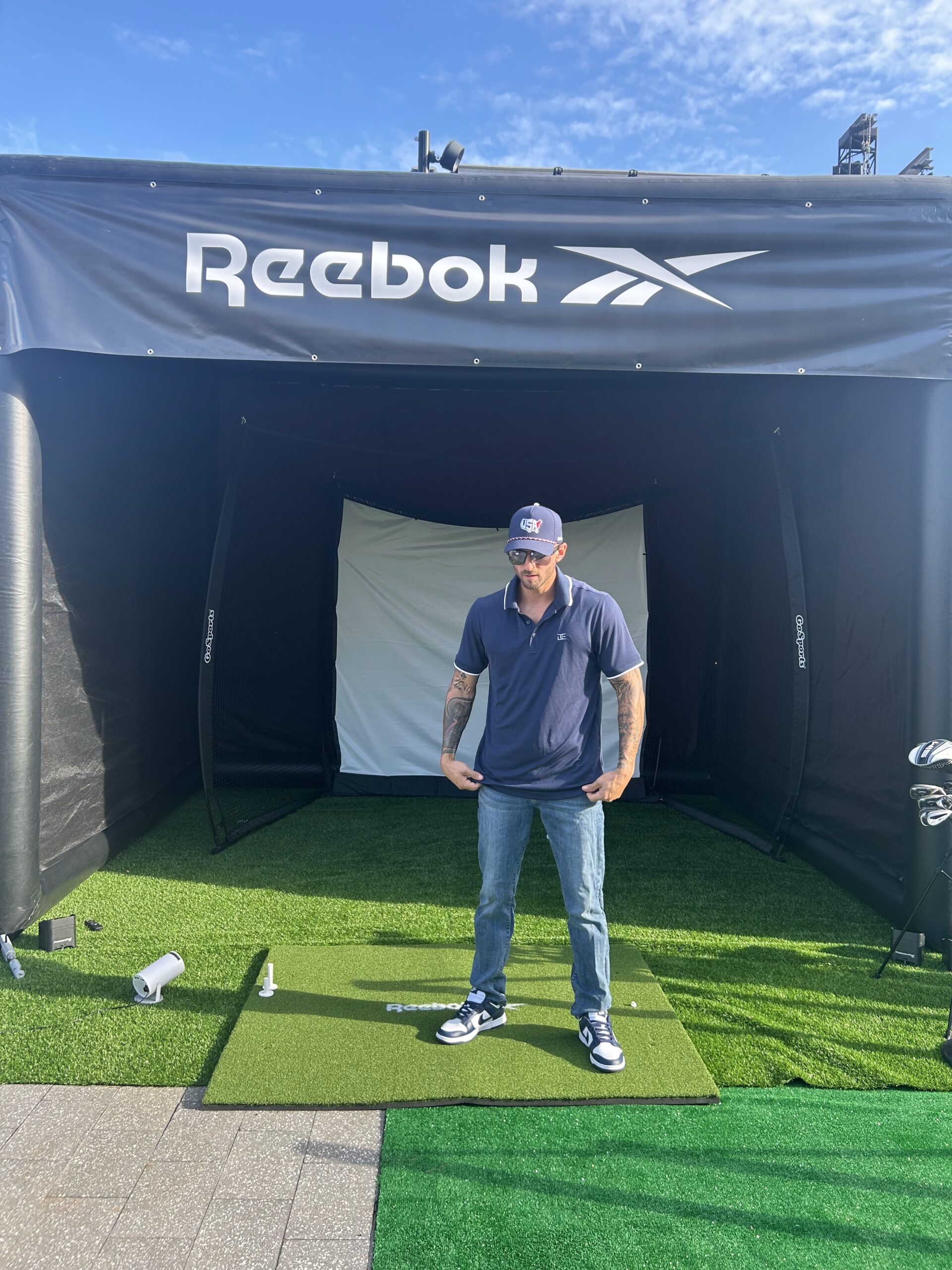 Man preparing to swing in a golf simulator setup branded with Reebok