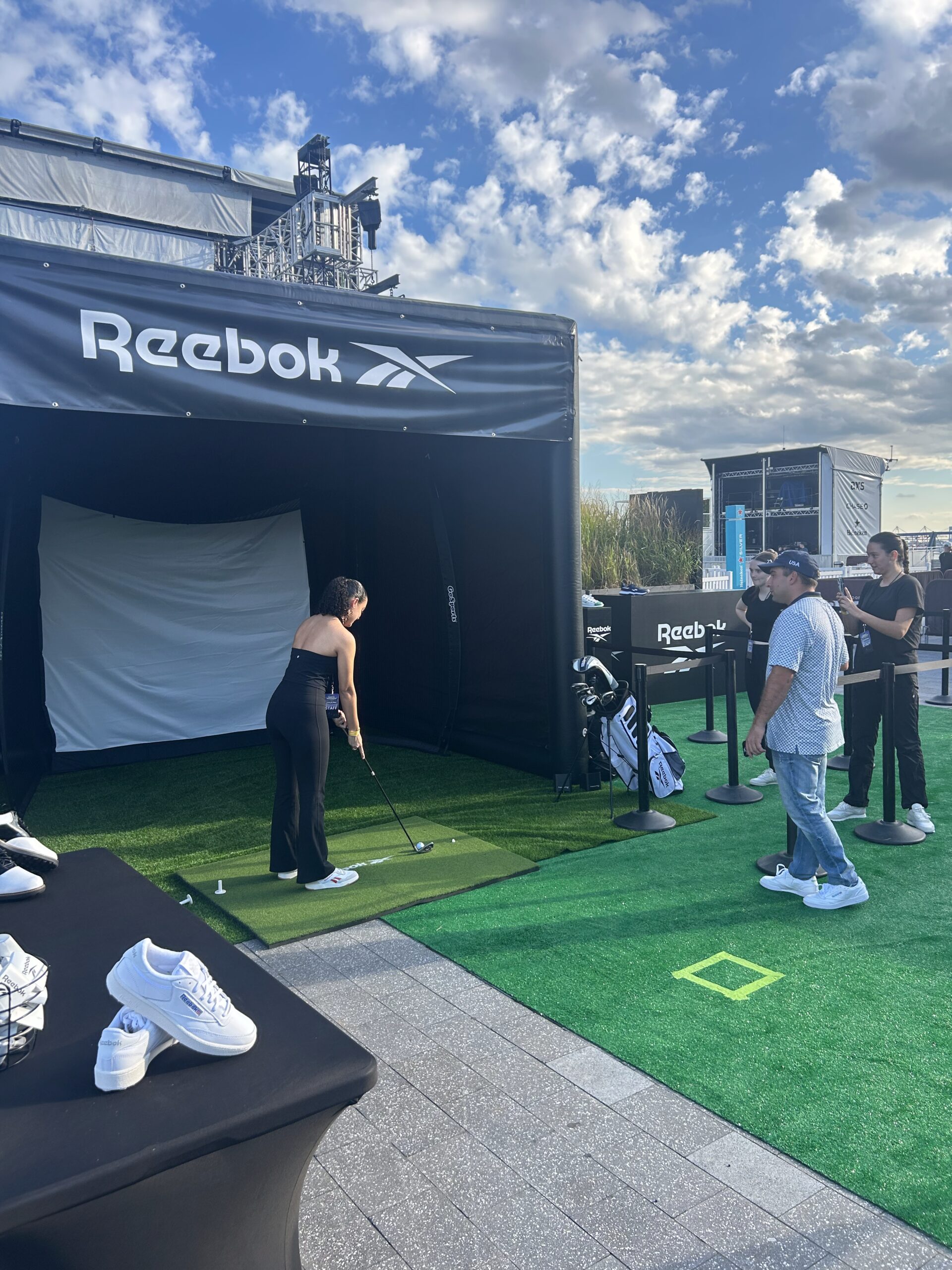 Woman preparing to swing golf club in Reebok-branded golf simulator