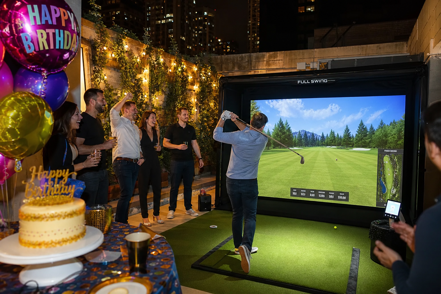 Group celebrating a birthday with a portable golf simulator, featuring a player swinging a club, surrounded by balloons and a birthday cake, in an outdoor setting with city lights.