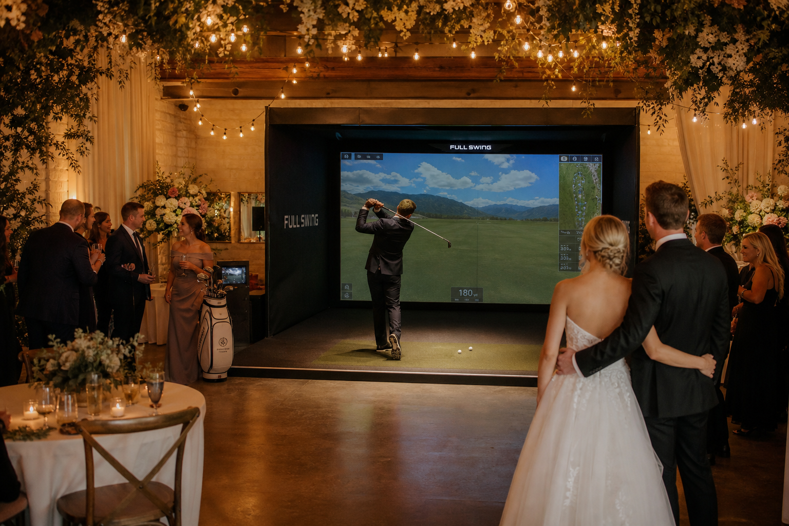 Golf simulator setup at a wedding reception, featuring a man swinging a club in front of a large screen displaying a golf course, surrounded by guests enjoying the event.