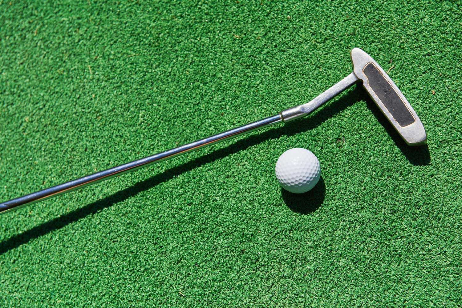 Golf putter and a white golf ball on artificial turf, representing indoor golfing experience at ParTee Golf in Manhattan.